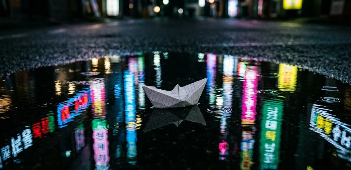 Um pequeno barco de papel flutuando em uma poça que reflete as luzes de uma metrópole estrangeira, representando o sentimento de isolamento, solidão e choque cultural.